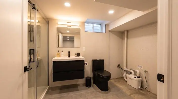 Salle de bain contemporaine aménagée au sous-sol d'une maison montréalaise avec éclairage artificiel soigné et système de pompe de relevage discrètement intégré pour évacuation sous le niveau de l'égout